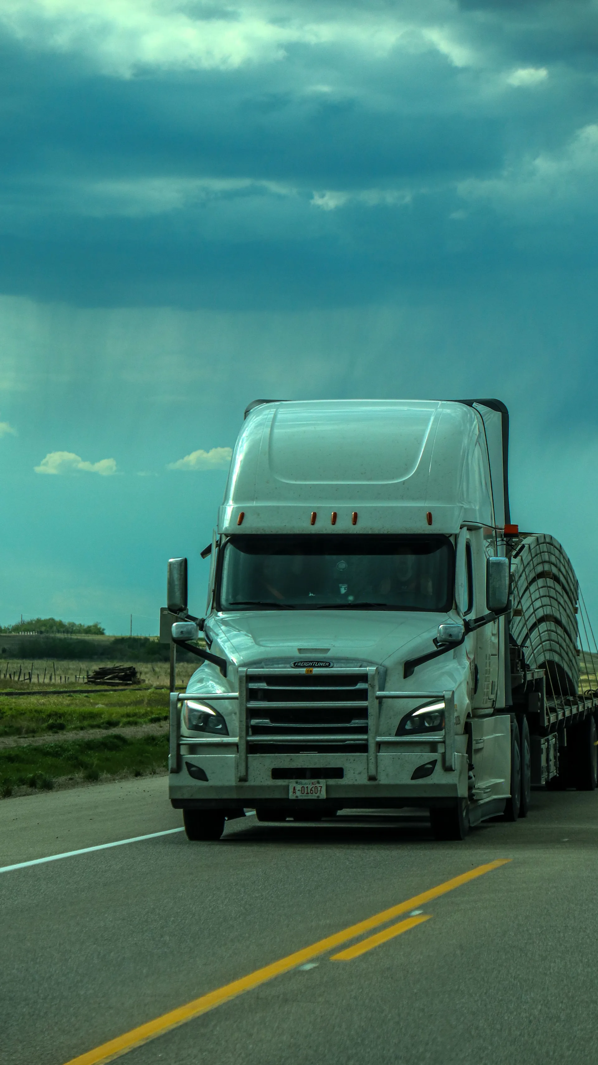 White SMARTWAY 95 flatbed semi truck driving under a stormy prairie sky