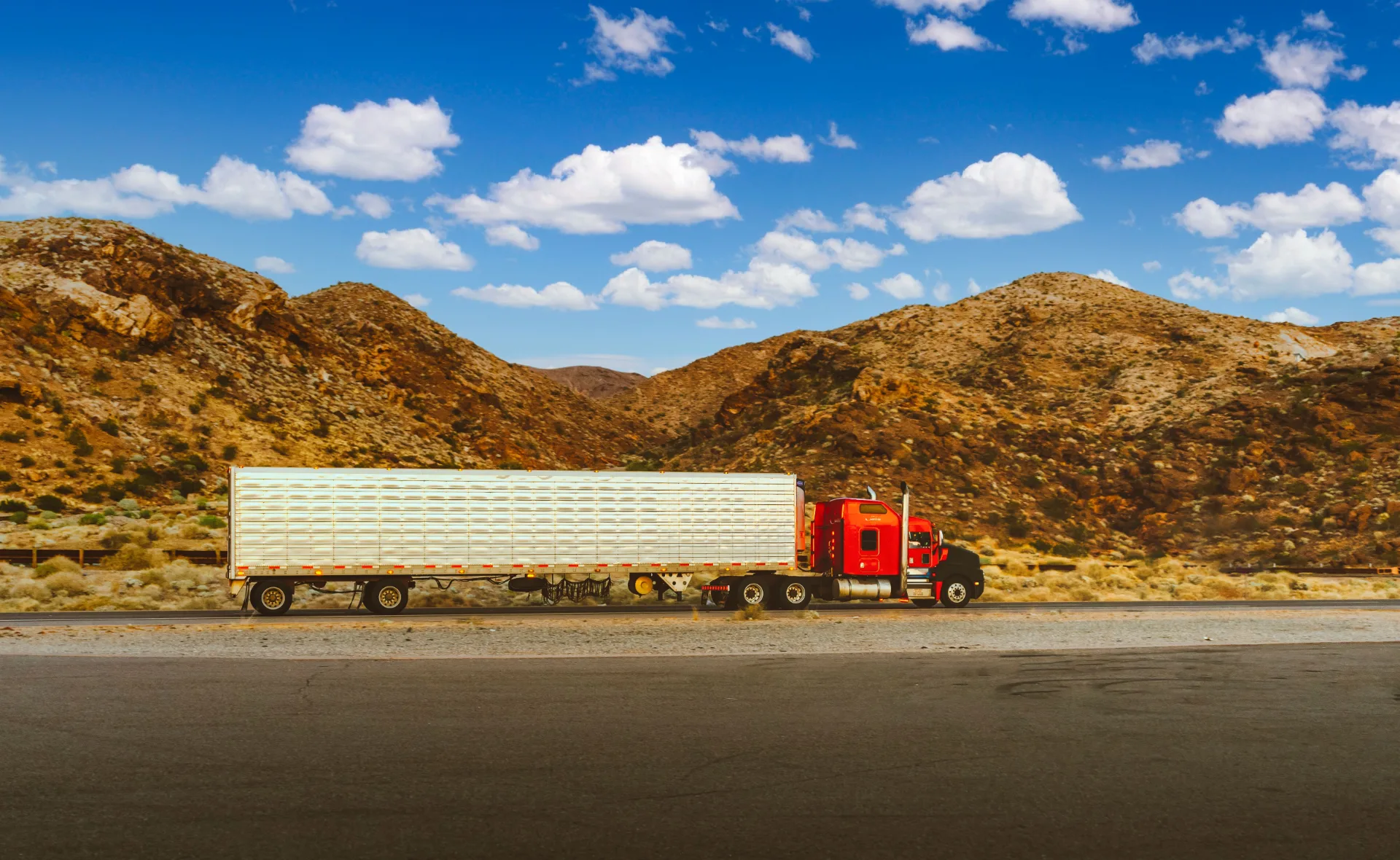 Red semi truck with refrigerated trailer parked in front of desert mountains